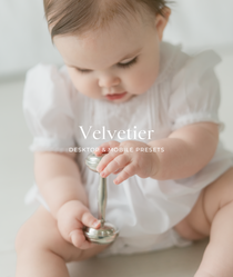 Baby in a white outfit holding a silver spoon with 'Velvetier' branding.